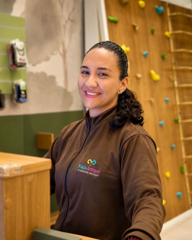 Monitora do FaçaAmigos sorrindo na recepção, com a parede de escalada ao fundo